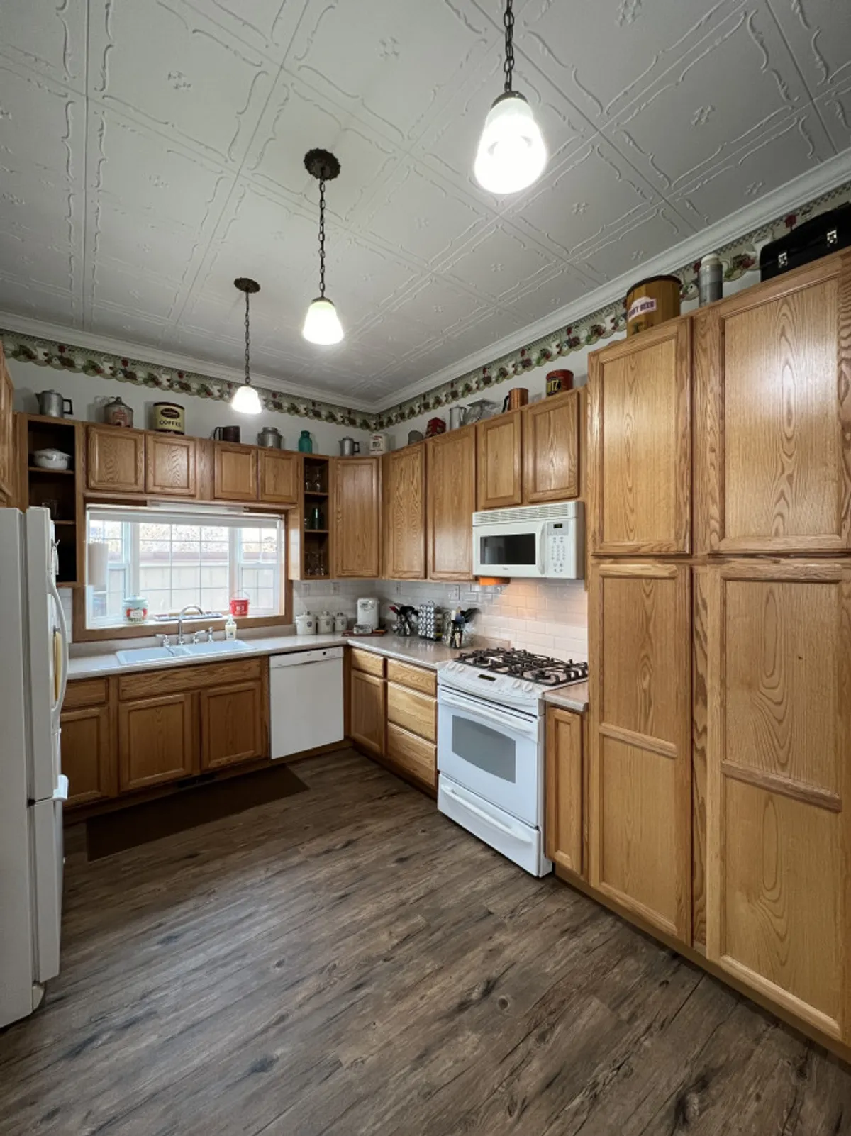 A cozy kitchen scene with upper and lower cabinets, a stove, a sink beneath a window, and charming decorative trim. The scene evokes the warmth and comfort of baking, family breakfasts, or preparing a feast together.