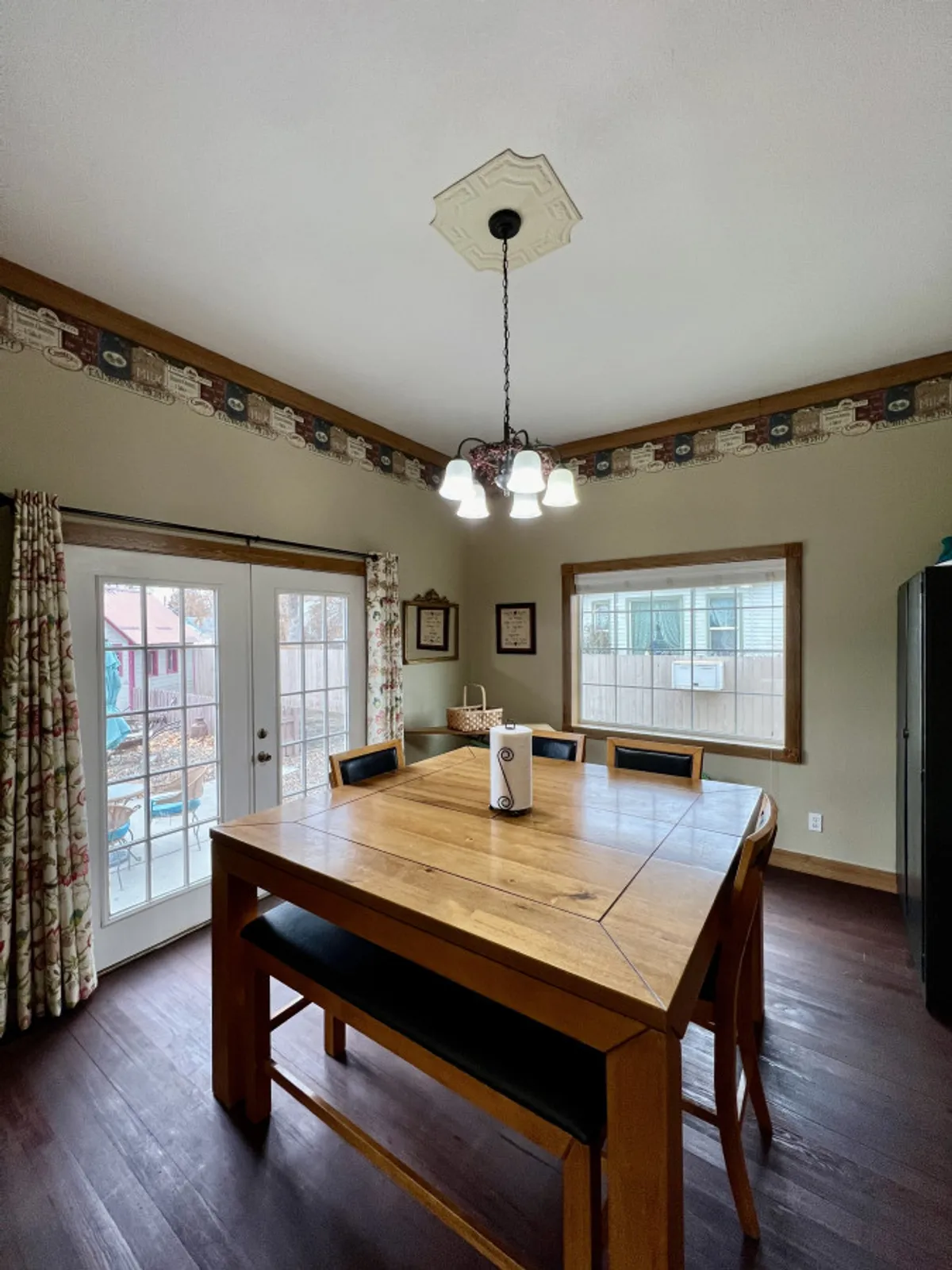 A spacious dining area with a large wooden table set under a chandelier, and a window that brings in natural light. The setting is ready for family meals, board games, or planning sessions, perfectly encapsulating communal dining.