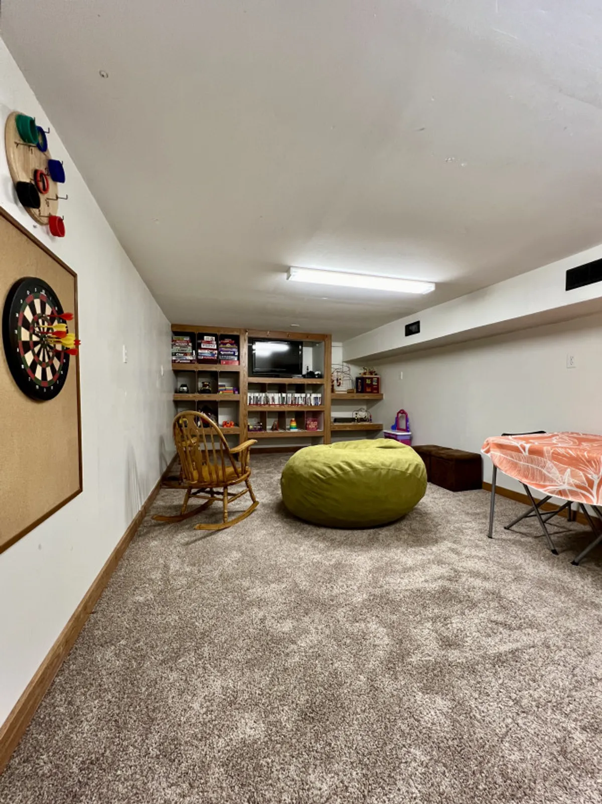 A relaxed and playful interior scene showcasing a dartboard, bean bag chair, and shelves stocked with games, designed for entertainment and casual group fun.