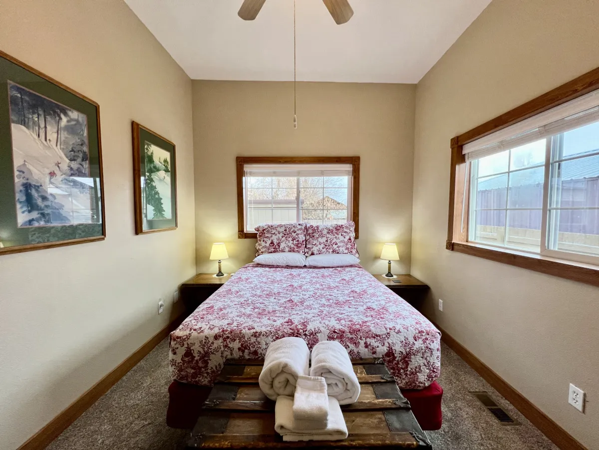 A tranquil bedroom featuring a bed with floral bedding, nightstands with lamps on either side, and a window that brings in natural light and offers a peaceful view. The soft colors and thoughtful arrangement evoke a sense of calm and relaxation, perfect for unwinding after an adventurous day.