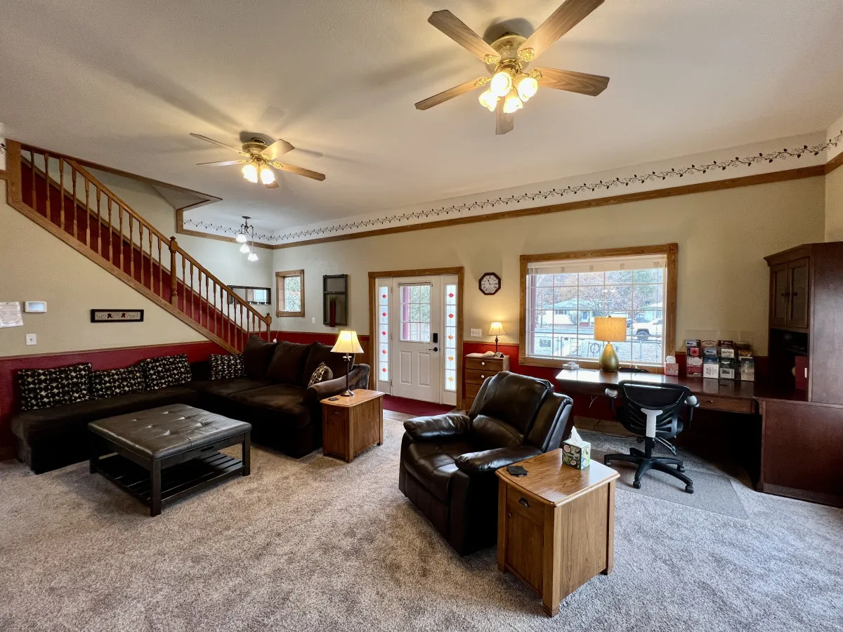 A cozy, spacious living space with a comfortable sectional sofa, leather recliner, a dining table with a lamp, and a decorative staircase. The layout suggests a perfect setting for movie nights, games, and quality family time.